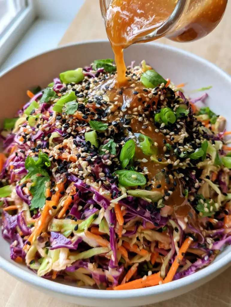 Asian Coleslaw Recipe with Glossy Ginger-Sesame Dressing 2 High-angle POV photo of a glossy ginger sesame dressing being poured over a mountain of shredded cabbage. (Asian coleslaw recipe)