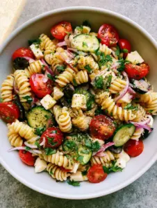 A smartphone photo of Italian pasta salad on a stone countertop with natural window lighting highlighting the rotini ridges.