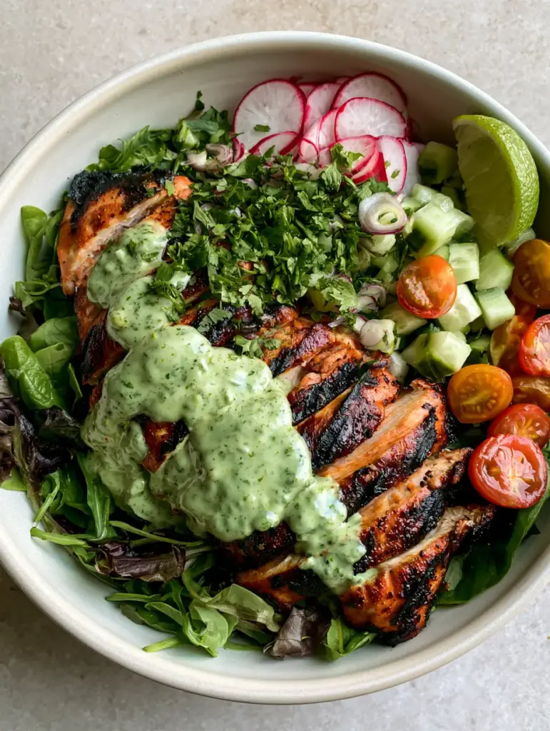 Peruvian Grilled Chicken Salad with Creamy Aji Verde Dressing 2 Close-up of charred chicken breast with dark grill marks over a bed of spring mix and spinach. (Peruvian Grilled Chicken Salad)