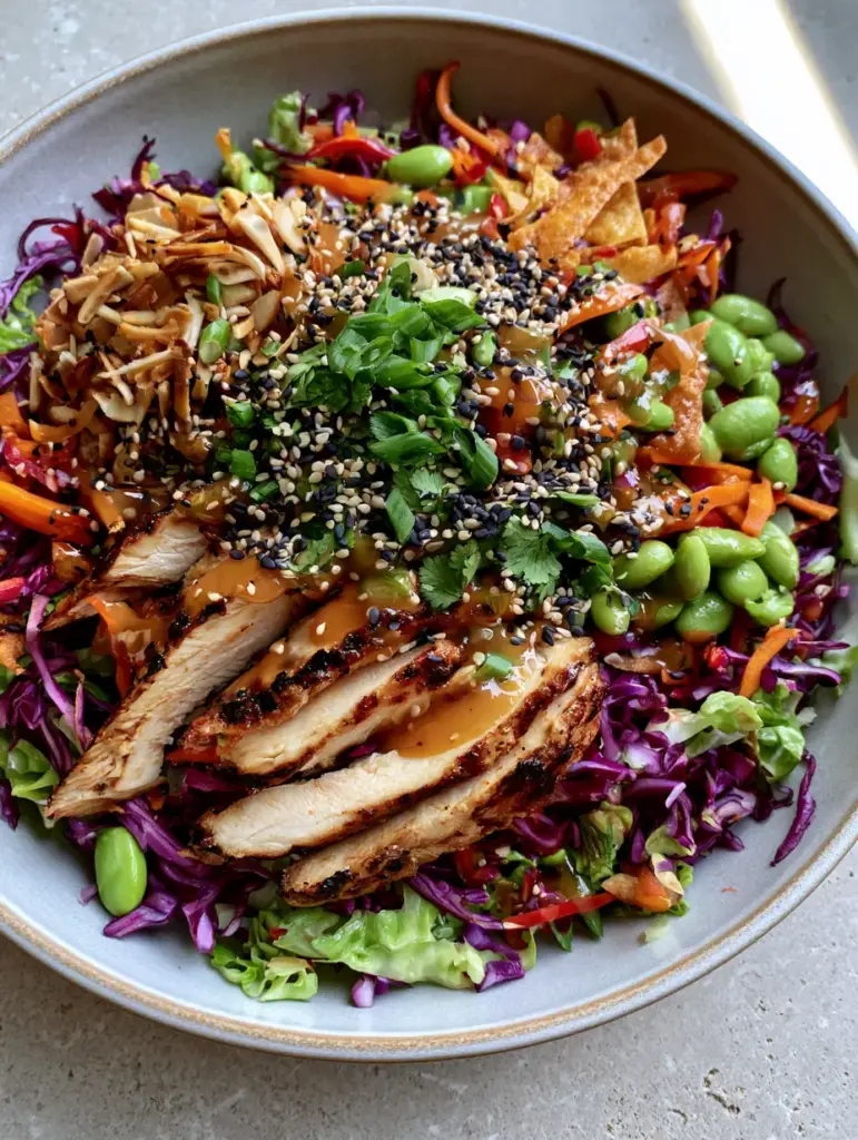 Crunchy Asian Chicken Salad with Ginger Sesame Dressing 2 Top-down view of a Crunchy Asian chicken salad with golden-brown chicken strips, matchstick carrots, and toasted almonds on a stone background.