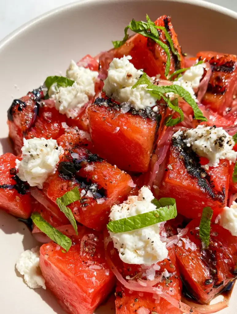 Grilled Watermelon with Feta and Mint: The Ultimate Savory-Sweet Summer Showstopper 1 A macro shot of Grilled Watermelon showing the texture of mint ribbons, red onion slivers, and flaky sea salt over ruby red fruit.