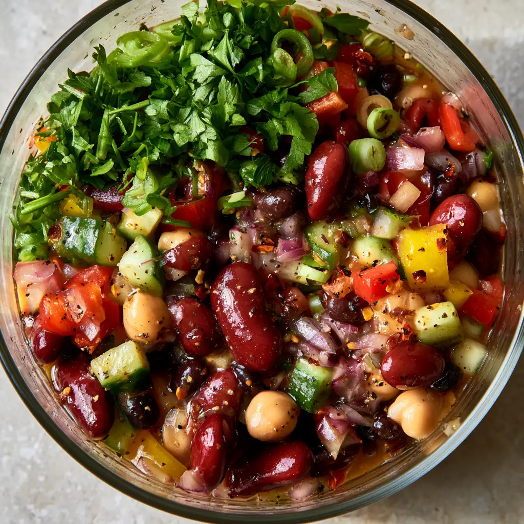 Top-down view of a glass bowl filled with colorful Marinated Bean Salad on a grey stone surface.