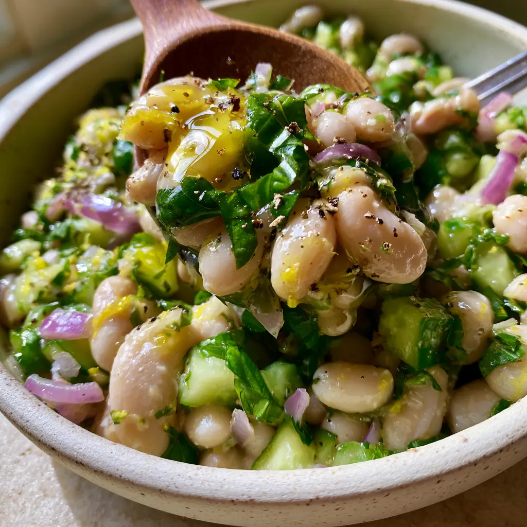 A wooden spoon lifting a portion of Lemon Basil Bean Salad with visible lemon zest and pepper.