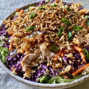 Macro shot of crunchy Ramen noodle chicken salad with golden-brown noodle crumbles and glossy dressing.