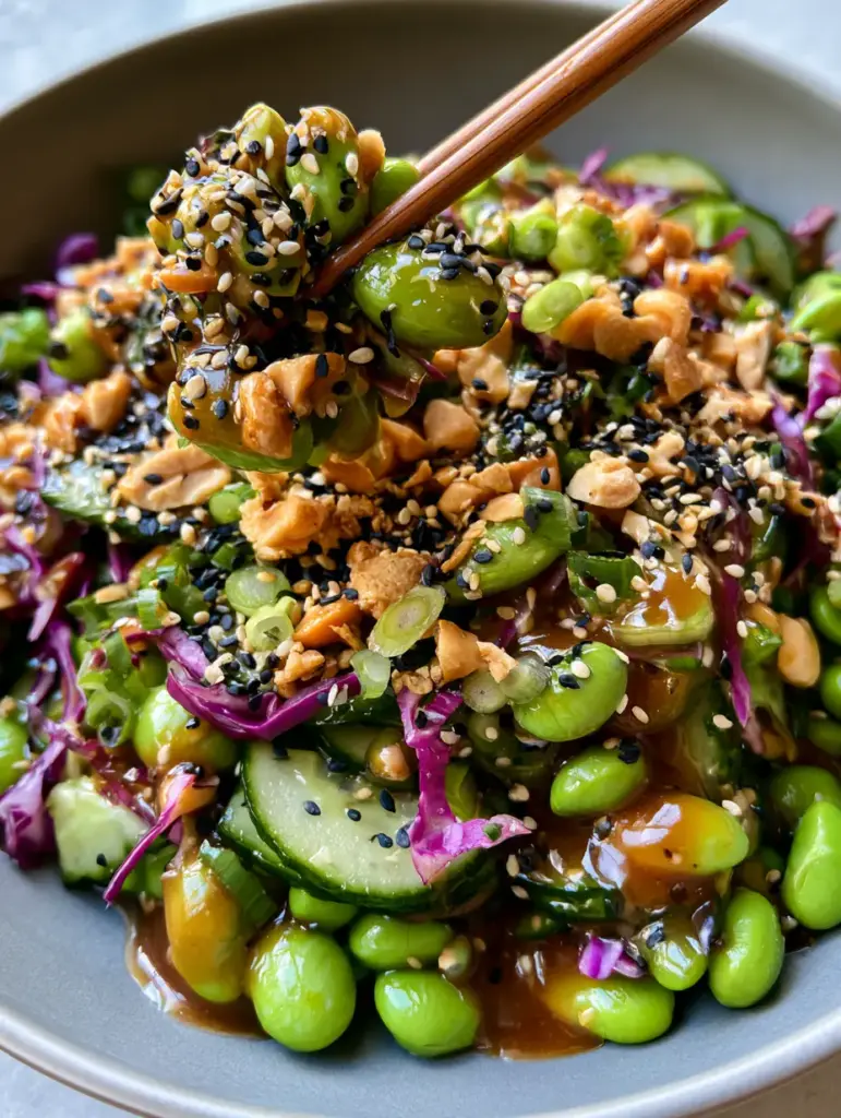 A close-up of Edamame and Cucumber Salad with one wooden chopstick lifting a cluster of cucumber and edamame.
