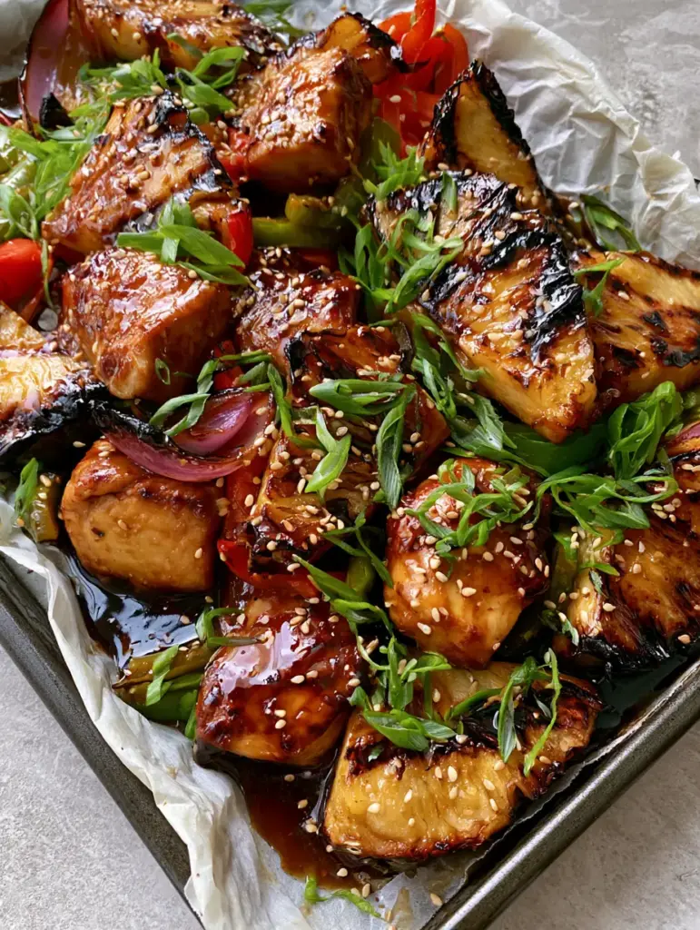 Charred pineapple wedges with distinct dark brown grill marks and red onion petals on a rustic metal pan for Gluten-free Hawaiian Chicken.