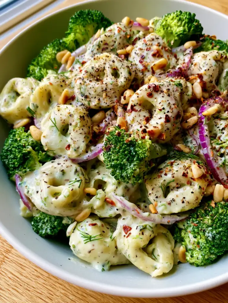 Tortellini Broccoli Salad with Zesty Herb Cream Dressing 1 Close up shot of emerald green blanched broccoli and cheese tortellini with toasted pine nuts. (Tortellini Broccoli Salad)
