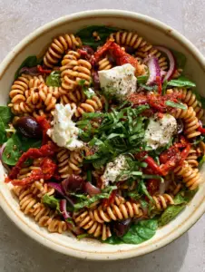 Close up of glossy rotini pasta in a Tuscan pasta salad with dark balsamic vinaigrette and basil garnish.