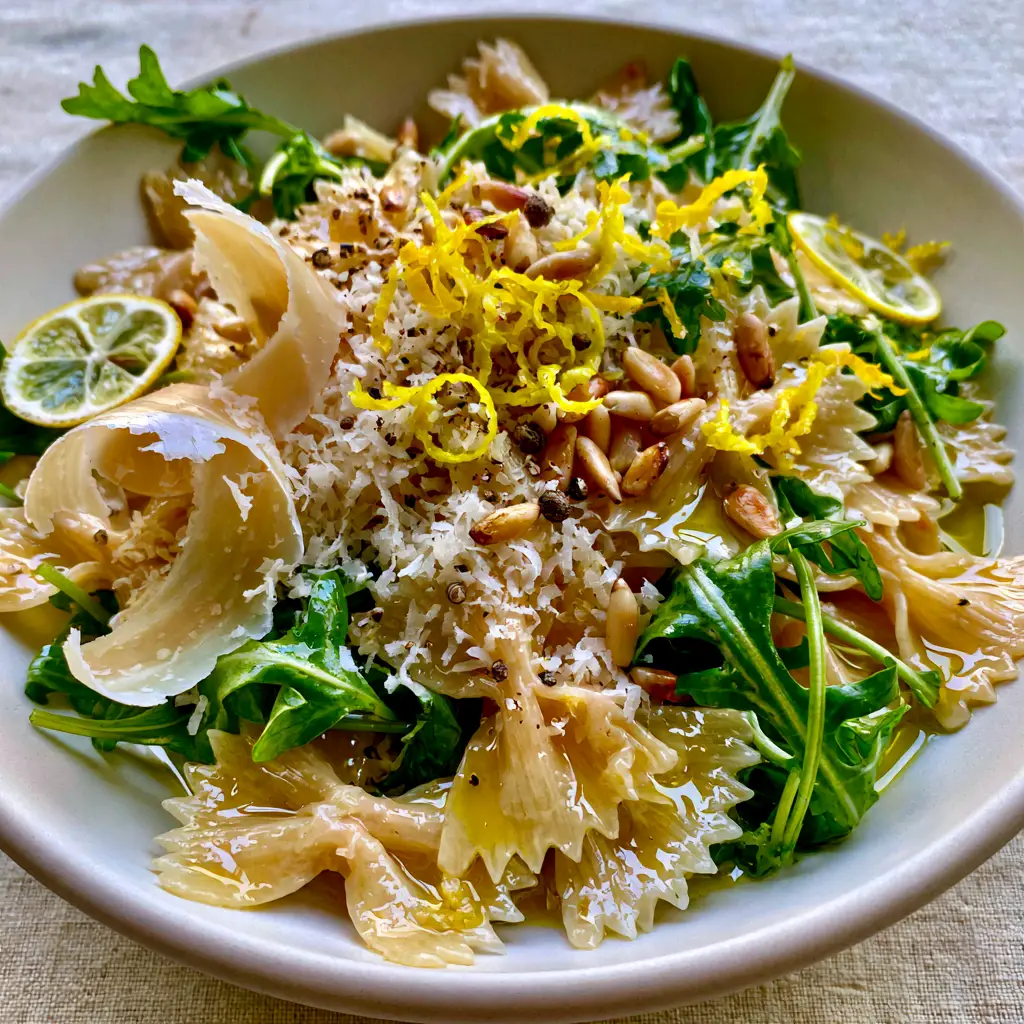 Lemon Parmesan Pasta Salad with Toasted Pine Nuts 1 Overhead view of pasta salad topped with toasted pine nuts, shaved parmesan, and thin lemon slices.